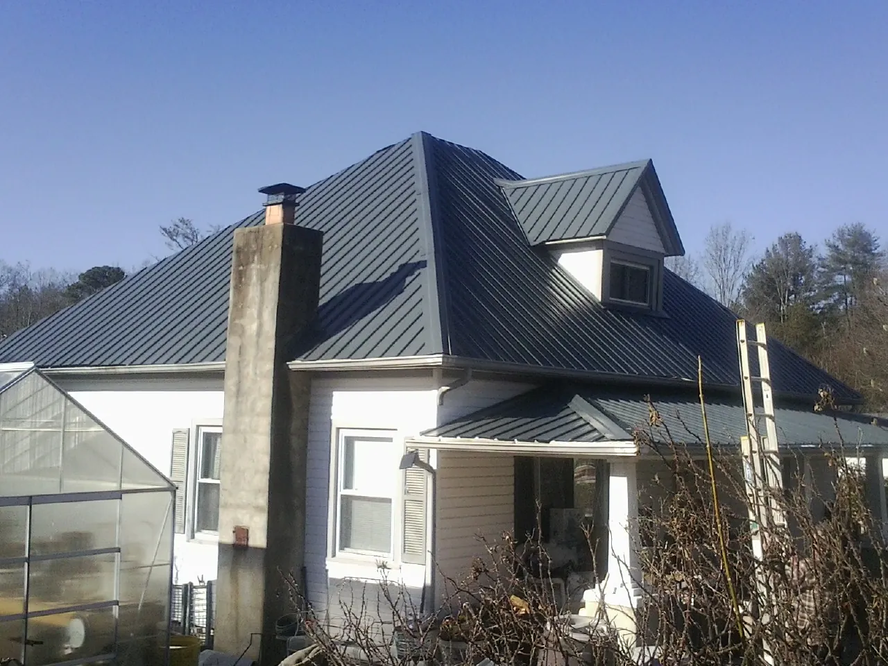 Dark blue standing seam metal roof on a white farmhouse with dormer — Slate & Tile Roof Repair by Roofing Brothers in Worley