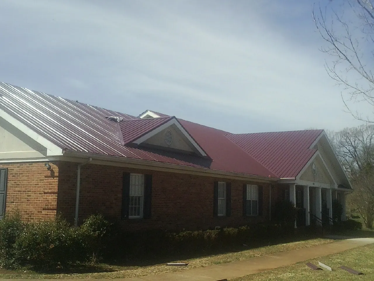 Red metal roof with gabled entries on a long brick building, from a Hail Damage Roof Repair job in Worley