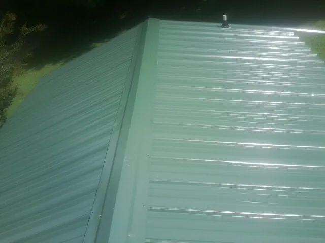 New green metal panels meeting at the ridge of a roof — Flat Roof Repair work by our crew in Worley