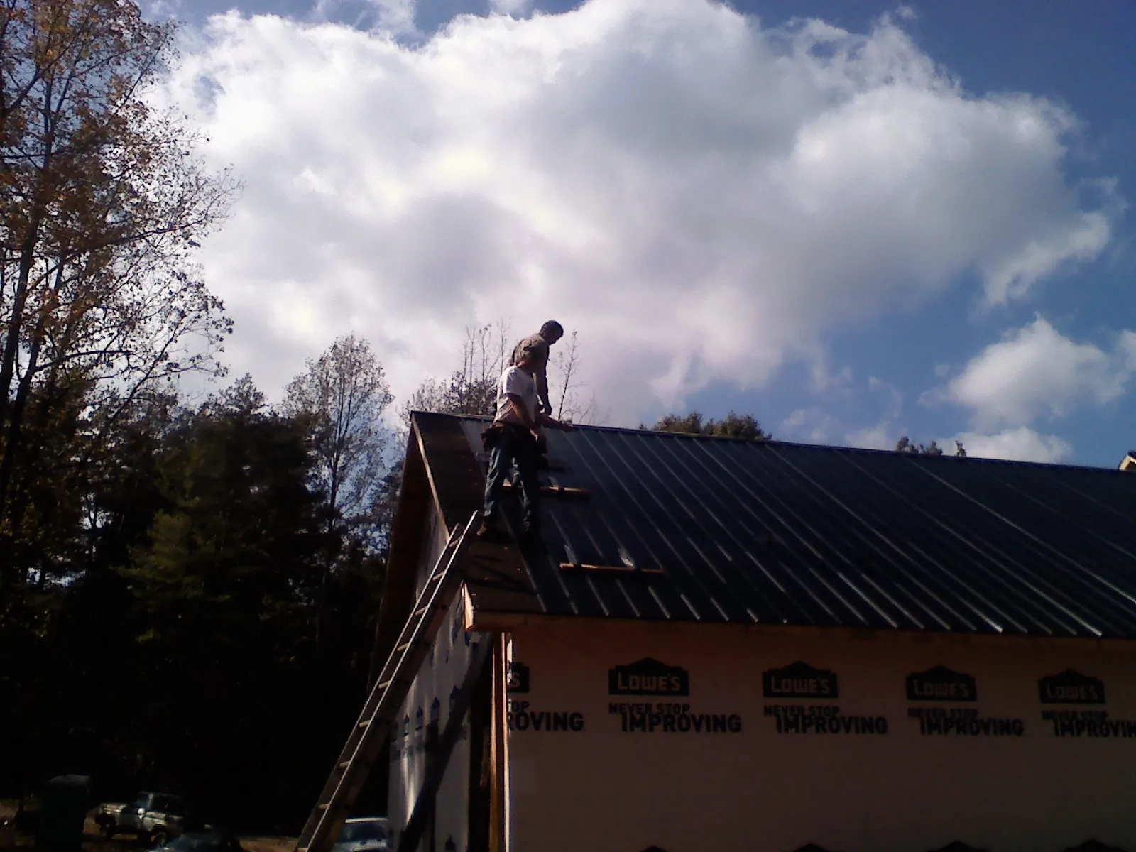 Roofer fastening dark metal panels high against a cloudy sky, from a Roof Inspection job in Worley