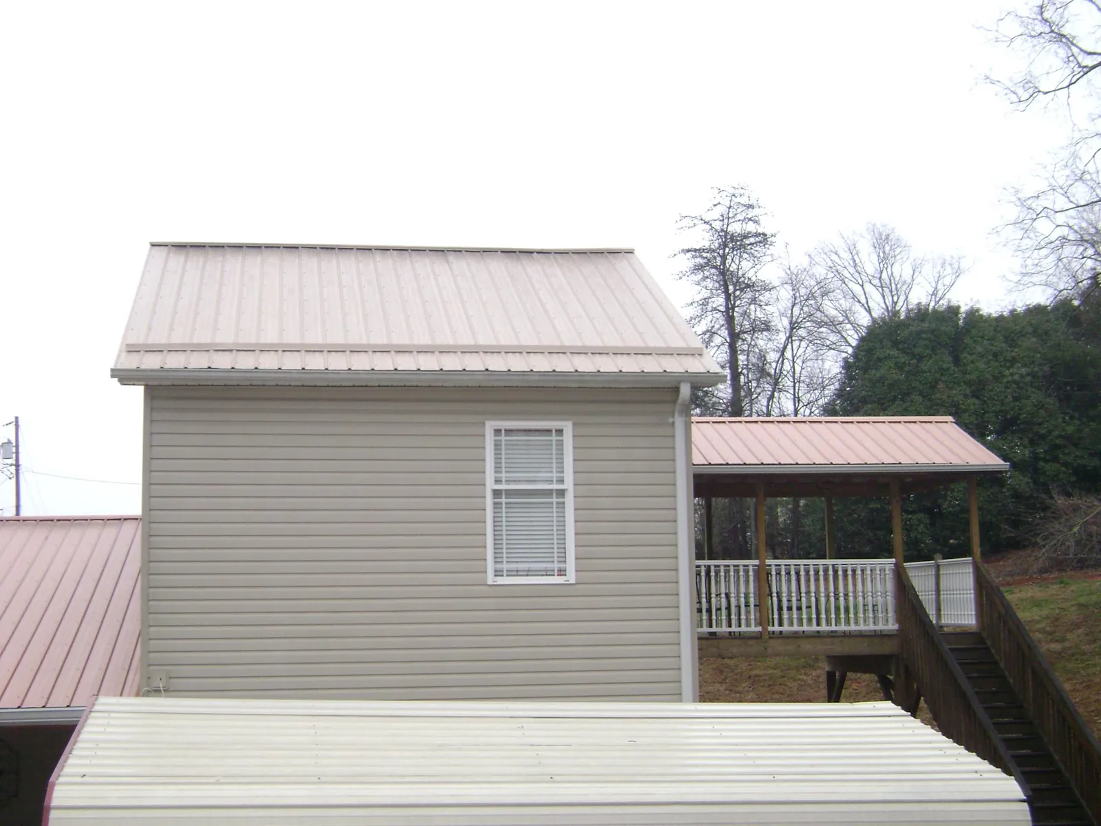 Tan metal roofs on a two story addition and attached porch in Worley